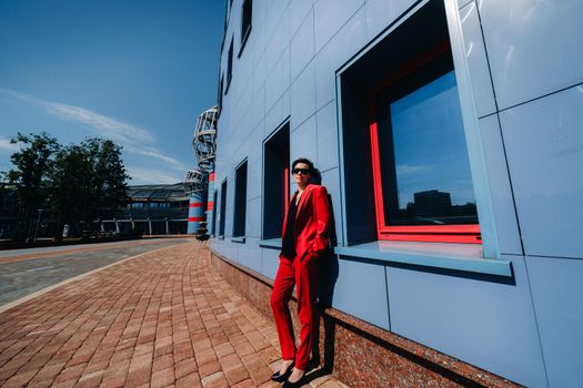 A girl in a red suit stands against the background of a modern building in the city.