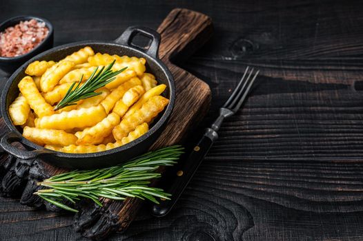 Fried Crinkle French fries potatoes in a pan. Black Wooden background. Top view. Copy space.