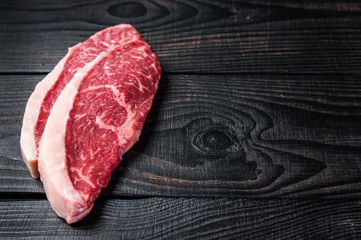 Raw rump steak or top sirloin cap beef meat steaks on butcher table. Black wooden background. Top view. Copy space.