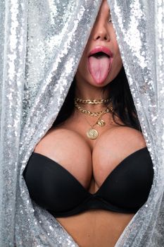 Portrait of a sexy brunette woman with big breasts dressed in a black bra peeking out from behind curtains of silver sequins