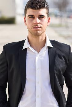 Young businessman near a modern office building wearing black suit and white shirt. Man with blue eyes