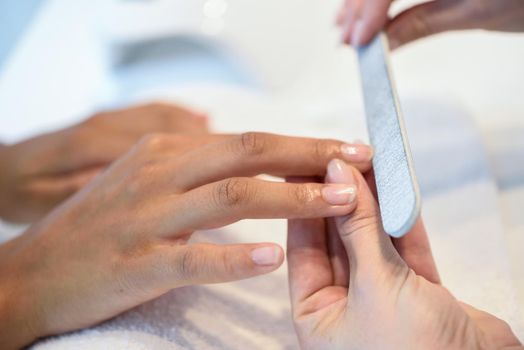 Close-up of a woman in a nail salon receiving a manicure by a beautician with. Beautician file nails to a customer.