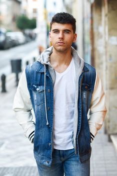 Good looking young man with blue eyes in the street. Model of fashion in urban background wearing white t-shirt, jeans and blue jacket