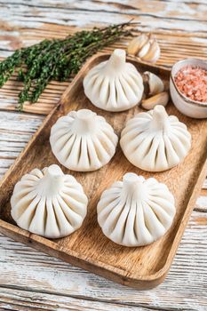 Frozen Raw dumplings Khinkali with beef and lamb meat on wooden tray with herbs. White wooden background. Top view.