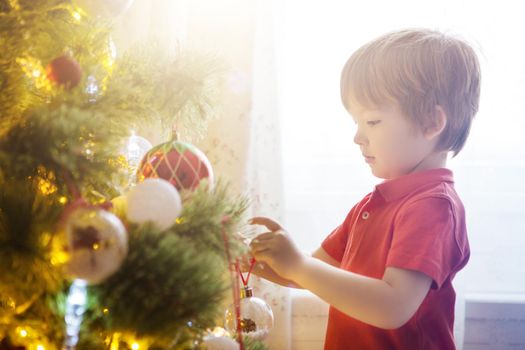 Happy child decorating the Christmas tree with balls. Christmas Eve concept.