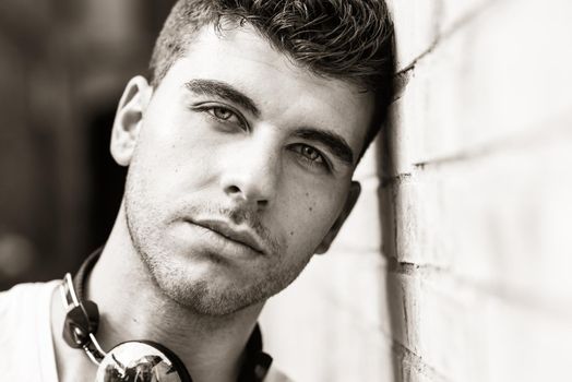 Portrait of young man in urban background listening to music with headphones. Wearing white t-shirt near a brick wall