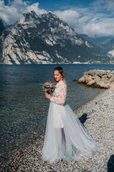 a girl in a smart white dress walks along the embankment of lake Garda.A woman is photographed against the background of a mountain and lake in Italy.Torbole.