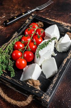 Ricotta cream Cheese in a wooden tray with basil and tomato. Dark background. Top view.