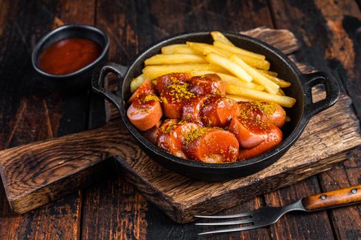 Currywurst Sausages with Curry spice on wursts served French fries in a pan. Dark wooden background. Top view.