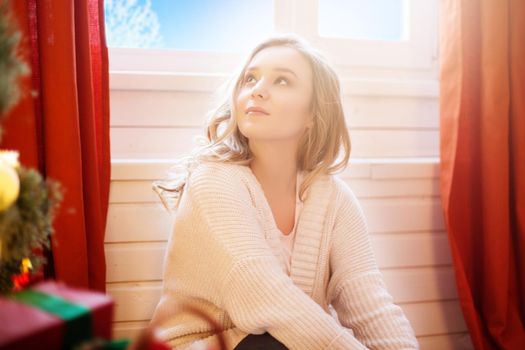 Beautiful young woman in white sweater sitting near christmas tree. Christmas photo.