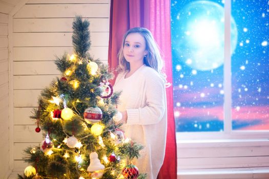 Woman decorating a Christmas tree. Christmas home room with tree and moon lighting in window. The elements of this image furnished by NASA.