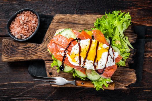 Smoked salmon Sandwich with Benedict egg and avocado on bread. Dark wooden background. Top view.