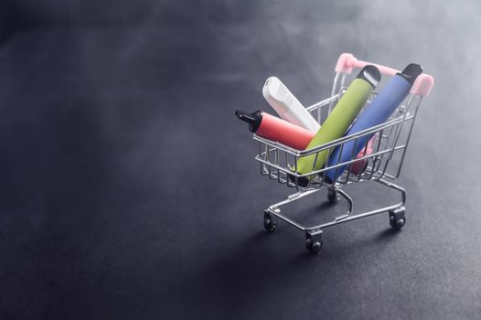 Disposable vapes in a shopping cart on a black background. Modern electronic cigarettes
