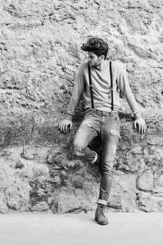 Portrait of young man wearing suspenders and blue jeans in urban background with modern haircut