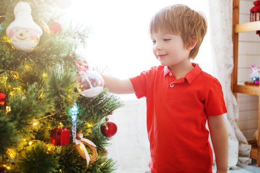 Little boy decorating the Christmas tree at home.