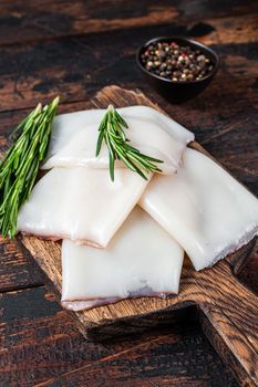 Raw Calamari or Squid on a wooden board with rosemary. Dark wooden background. Top view.