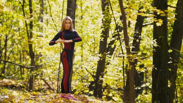 Woman doing fitness exercises outdoor. Female stretching in autumn forest. Slim girl at outdoor workout, telephoto