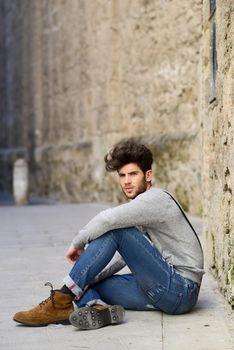 Portrait of young man wearing suspenders sitting on the floor in urban background