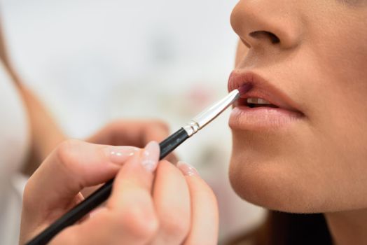 Makeup artist making up lips of an African young woman in a beauty center.. Beauty and Aesthetic concepts.