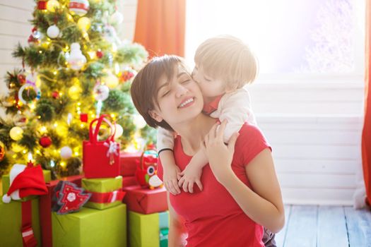 Smiling mother with her little son in living room decorated for Christmas. Son embracing his mother.