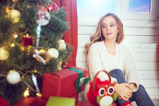 Happy woman sitting near Christmas tree at home.