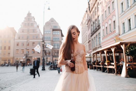 A bride in a wedding dress with long hair and a drink bottle in the Old town of Wroclaw. Wedding photo shoot in the center of an old Polish city.Wroclaw, Poland.