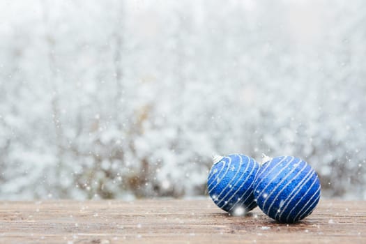 Beautiful Christmas bauble decorations lie on the wooden table over snow covered forest background. .