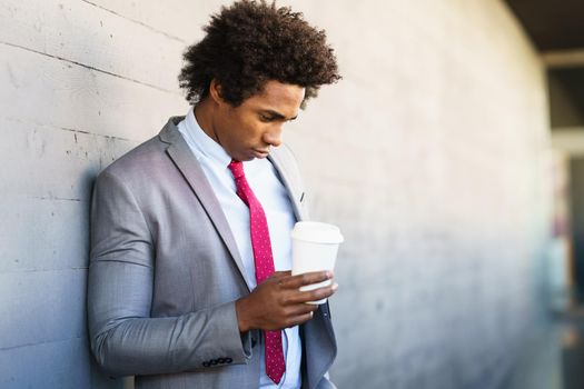 Worried Black Businessman taking a coffee break with a take-away glass. Man with afro hair.