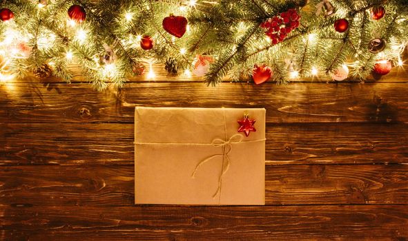 Blurred Christmas background, with fir branches, fairy lights, gift box and christmas decorations on brown wooden plank .