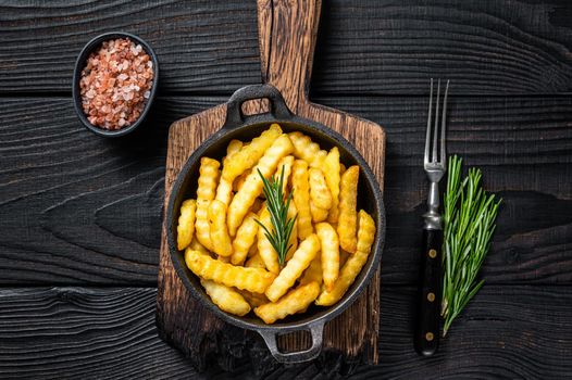 Fried Crinkle French fries potatoes in a pan. Black Wooden background. Top view.