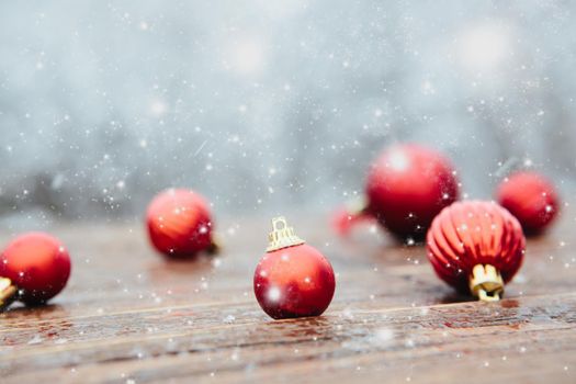 Red balls on board place snow and landscape of tree. Beautiful Christmas bauble decorations lie on the wooden table over snow covered forest background. Atmosphere of magic and fairy tales .