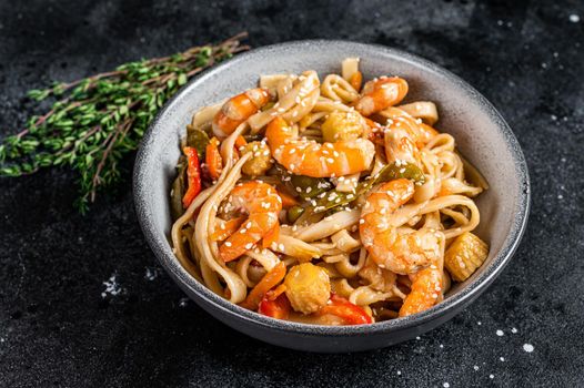 Chinese wok Stir-fry udon seafood noodles with shrimp prawns in a bowl. Black background. Top view.