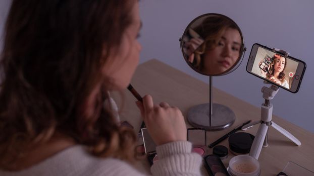 Caucasian woman leads an online make-up lesson for herself on her mobile phone.