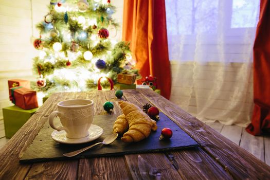 Mug with hot chocolate on a wooden table with Christmas decorations on a background of the Christmas tree .