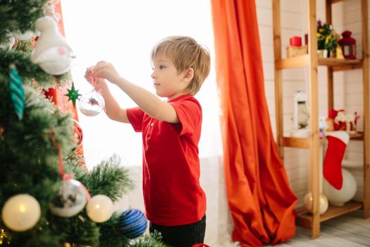 Cute little boy of about five year with blue eyes decorating a Christmas tree. .