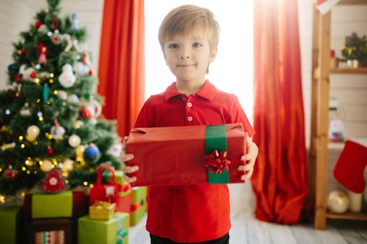 Cute little boy of about five year with a gift in a decorated Christmas room with a xmas tree. .