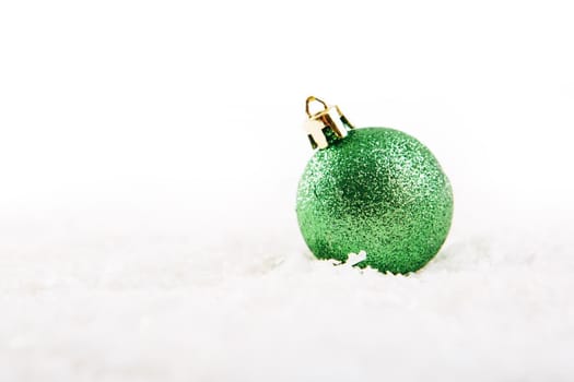 Green christmas ball on snow over white background .