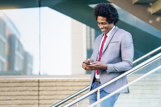 Smiling Black Businessman using his smartphone near an office building. Man with afro hair.