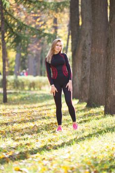 Young fitness beauty girl during workout standing near trees at autumn park, telephoto