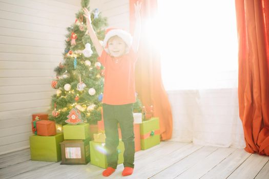 Little cute boy with blue eyes in a Santa Claus hat in a decorated Christmas room with a xmas tree. .