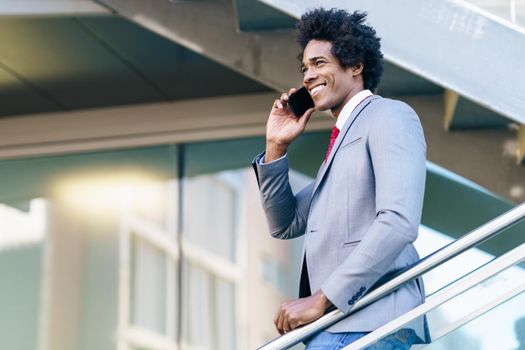 Smiling Black Businessman using his smartphone near an office building. Man with afro hair.