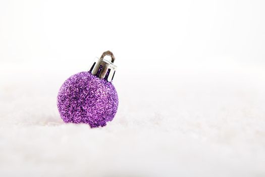 Lilac or purple christmas ball on snow over white background .