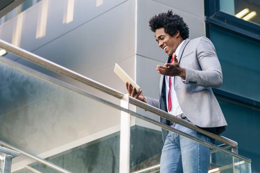 Black Businessman using a digital tablet sitting near an office building. Man with afro hair.