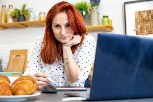 Woman using laptop while sitting at home. Young woman sitting in kitchen and working on laptop. remote work