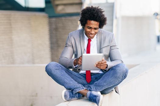 Black Businessman using a digital tablet sitting near an office building. Man with afro hair.