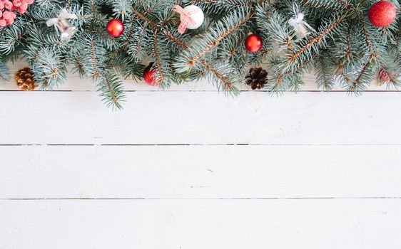 Christmas fir tree on wooden board background with copy space. Blurred Christmas background, with fir branches, fairy lights and christmas decorations on white wooden plank .