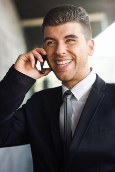 Attractive young businessman on the phone in an office building wearing black suit and tie. Man with blue eyes