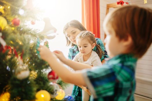 Happy family mom, son and daughter on a Christmas winter sunny morning in a decorated Christmas celebration room with a Xmas tree and gifts. .