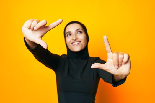 Muslim in black hijab posing fashion hand gesture yellow background. High quality photo
