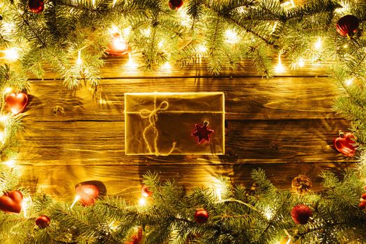 Blurred Christmas background, with fir branches, fairy lights, gift box and christmas decorations on brown wooden plank .